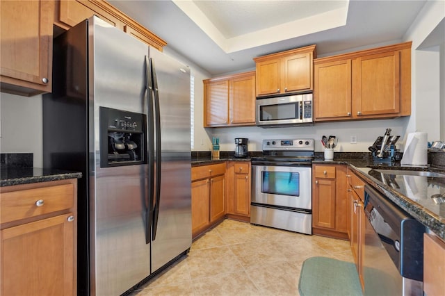 456 Bahia Beach Blvd, Ruskin, FL 33570 - kitchen featuring dark stone countertops, light tile patterned floors, a tray ceiling, brown cabinetry, and appliances with stainless steel finishes