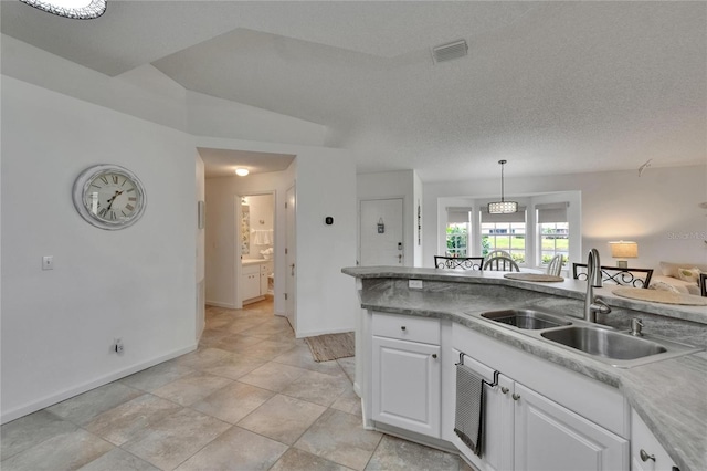 kitchen featuring visible vents, baseboards, white cabinetry, a sink, and hanging light fixtures