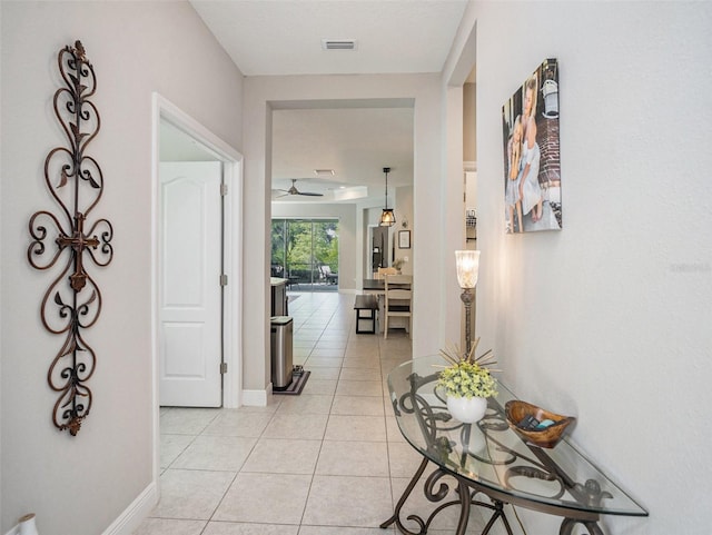 corridor featuring baseboards, visible vents, and light tile patterned floors