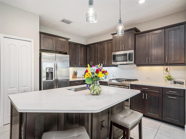 kitchen featuring a kitchen breakfast bar, dark brown cabinetry, backsplash, appliances with stainless steel finishes, and visible vents