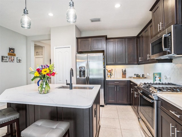 kitchen featuring stainless steel appliances, backsplash, a sink, light stone countertops, and dark brown cabinetry