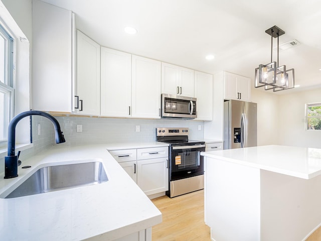 kitchen with a sink, decorative light fixtures, light wood-type flooring, tasteful backsplash, and appliances with stainless steel finishes