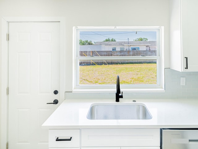 kitchen with stainless steel dishwasher, tasteful backsplash, a sink, light countertops, and white cabinets