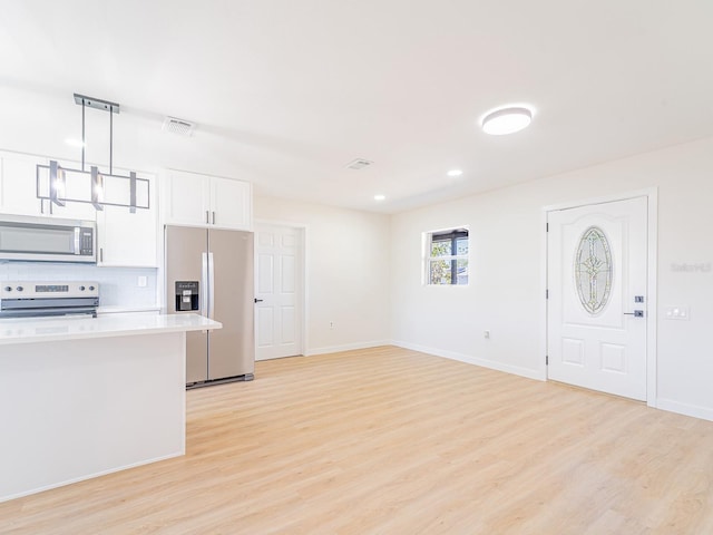 interior space featuring light countertops, white cabinetry, appliances with stainless steel finishes, light wood finished floors, and pendant lighting