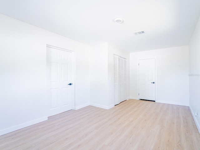 empty room with light wood-style floors, visible vents, and baseboards