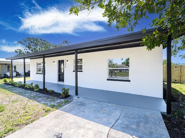 view of front of house with covered porch, stucco siding, and fence