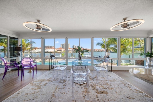 sunroom / solarium with a textured ceiling, wood finished floors, and a water view
