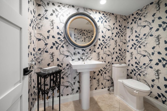 bathroom with toilet, wallpapered walls, baseboards, and tile patterned flooring