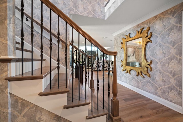 stairs featuring baseboards, wallpapered walls, crown molding, and wood finished floors