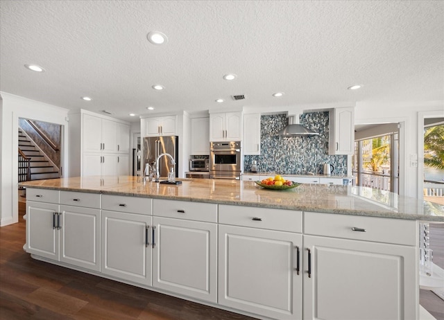 kitchen with visible vents, wall chimney exhaust hood, a textured ceiling, and appliances with stainless steel finishes