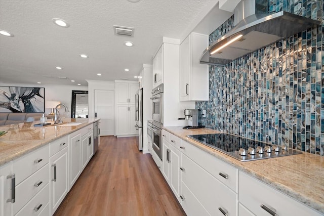 kitchen with wall chimney range hood, visible vents, wood finished floors, a sink, and stainless steel appliances