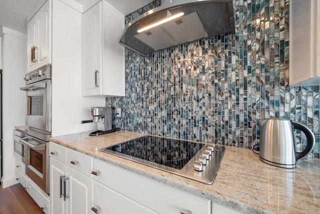 kitchen with range hood, light stone counters, backsplash, black electric cooktop, and double oven