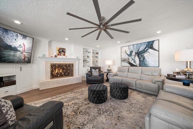 living area featuring ornamental molding, a textured ceiling, wood finished floors, ceiling fan, and a premium fireplace