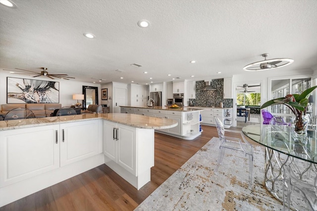 kitchen with a ceiling fan, a textured ceiling, stainless steel appliances, dark wood-type flooring, and a kitchen island