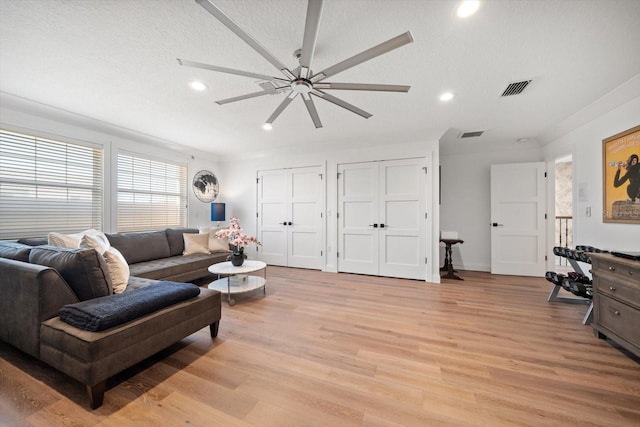 living area with light wood-style floors, a textured ceiling, a ceiling fan, visible vents, and recessed lighting