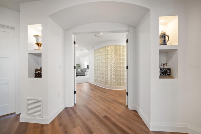 hall featuring visible vents, built in features, arched walkways, and baseboards