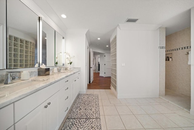full bath with visible vents, a sink, a walk in shower, double vanity, and tile patterned flooring