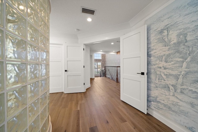 hallway with visible vents, wallpapered walls, wood finished floors, and an upstairs landing