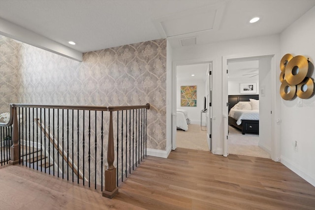 hallway with an upstairs landing, baseboards, wallpapered walls, and wood finished floors