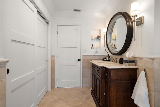 bathroom featuring vanity, tile patterned floors, visible vents, wainscoting, and tile walls