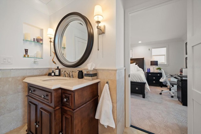 ensuite bathroom with ornamental molding, tile walls, ensuite bath, vanity, and wainscoting