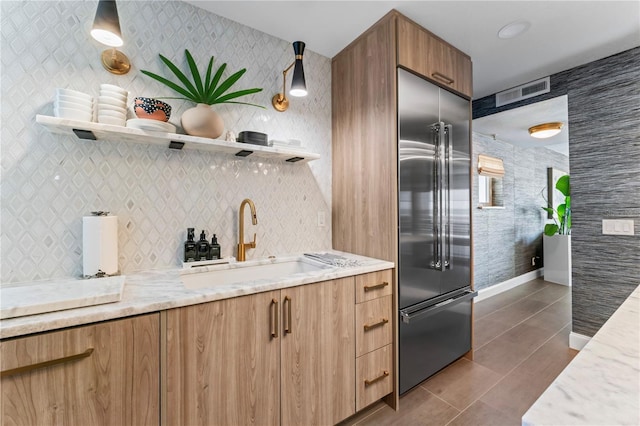 kitchen with built in refrigerator, a sink, open shelves, and light stone counters