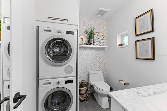 bathroom with vanity, stacked washer and dryer, tile patterned floors, toilet, and tile walls
