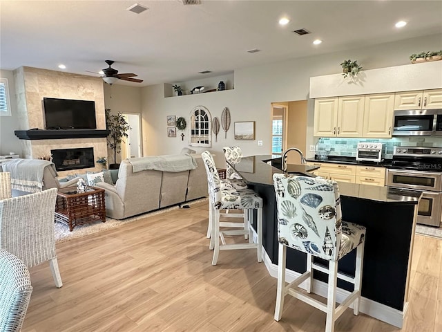kitchen featuring ceiling fan, dark countertops, a kitchen breakfast bar, light wood finished floors, and stainless steel appliances