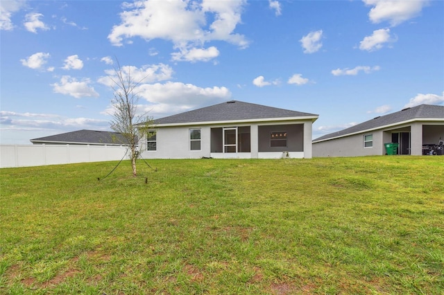 rear view of property featuring a lawn, stucco siding, a sunroom, and fence