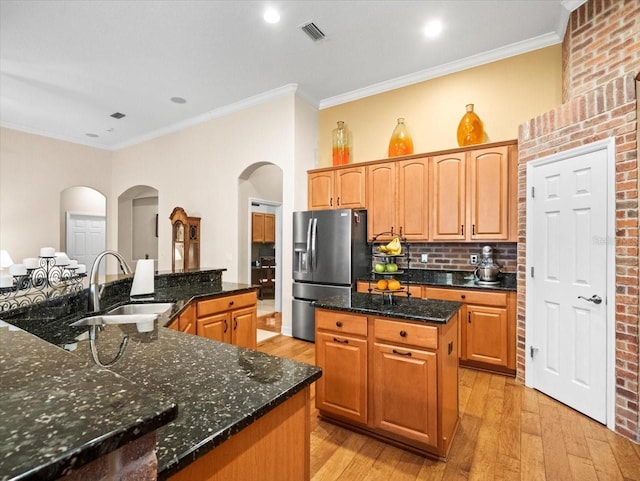 kitchen with stainless steel fridge with ice dispenser, visible vents, a center island, arched walkways, and a sink
