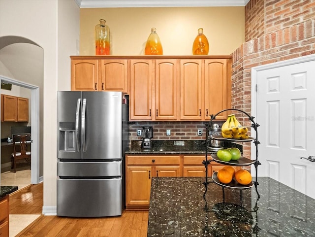kitchen with stainless steel fridge, crown molding, light wood-style floors, dark stone counters, and arched walkways