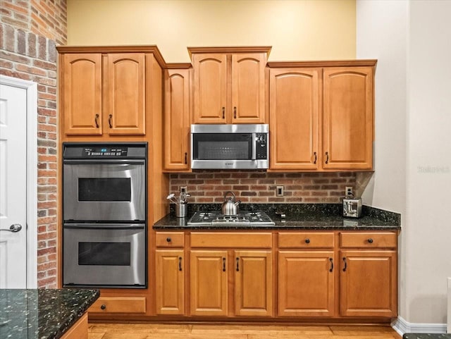 kitchen featuring dark stone countertops, light wood-style flooring, decorative backsplash, and stainless steel appliances