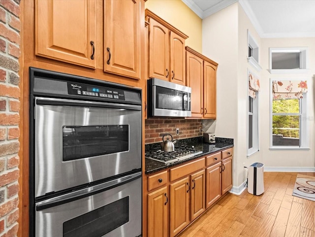 kitchen featuring dark stone countertops, light wood-style flooring, appliances with stainless steel finishes, crown molding, and decorative backsplash