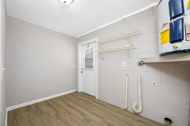 washroom with baseboards, laundry area, wood finished floors, and water heater