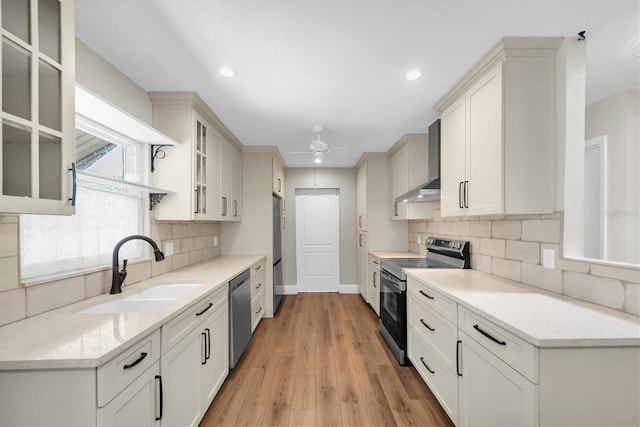 kitchen featuring tasteful backsplash, light wood-style floors, wall chimney exhaust hood, appliances with stainless steel finishes, and a sink
