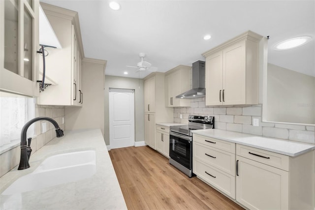 kitchen with wall chimney exhaust hood, a sink, stainless steel electric stove, a ceiling fan, and backsplash