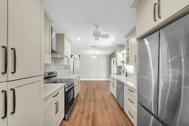 kitchen featuring baseboards, wall chimney range hood, ceiling fan, light countertops, and stainless steel appliances
