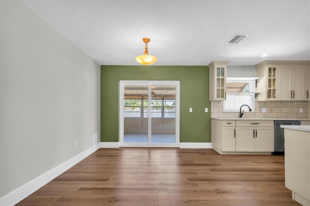kitchen with stainless steel dishwasher, glass insert cabinets, visible vents, light countertops, and backsplash
