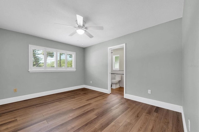 unfurnished bedroom with wood finished floors, ensuite bathroom, baseboards, and a ceiling fan