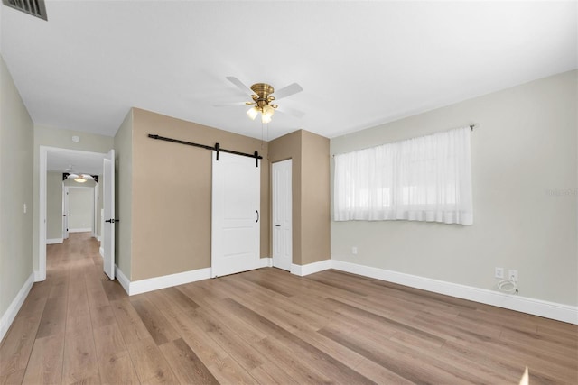 unfurnished bedroom featuring ceiling fan, visible vents, a barn door, wood finished floors, and baseboards