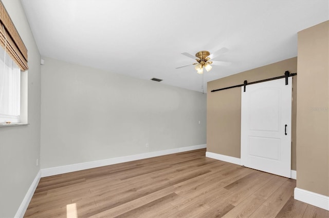 unfurnished bedroom with visible vents, baseboards, a barn door, ceiling fan, and light wood-style flooring
