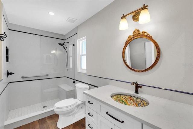 full bath featuring tiled shower, vanity, visible vents, toilet, and wood finished floors