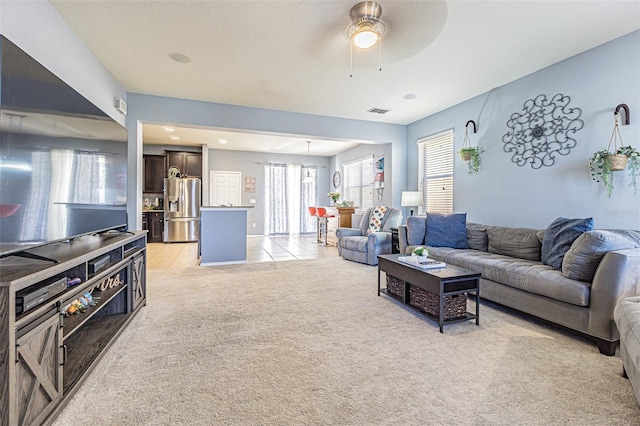 living area with light tile patterned flooring, light colored carpet, ceiling fan, and visible vents