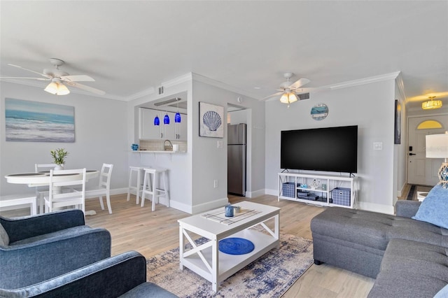 living room with crown molding, baseboards, a ceiling fan, and light wood-type flooring