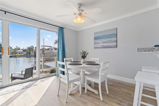 dining area with crown molding, baseboards, ceiling fan, a water view, and light wood finished floors