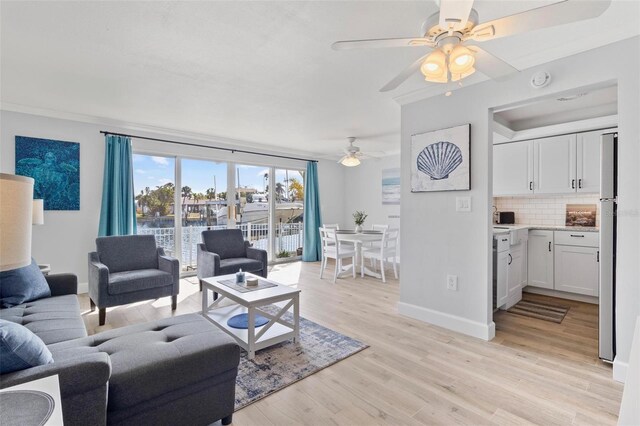 living area with baseboards, ornamental molding, a ceiling fan, and light wood-style flooring