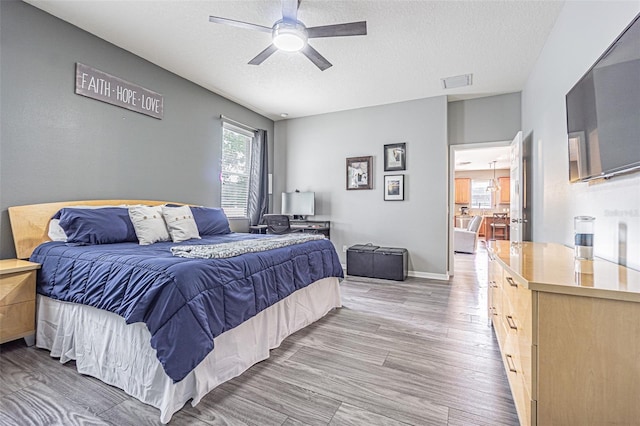 bedroom with ceiling fan, a textured ceiling, light wood-style flooring, and visible vents