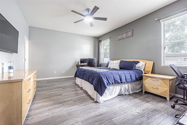 bedroom featuring a textured ceiling, baseboards, wood finished floors, and a ceiling fan