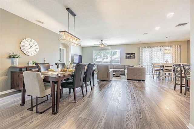 dining space with a textured ceiling, visible vents, wood finished floors, and ceiling fan with notable chandelier