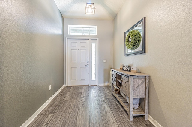 foyer entrance with a textured wall, baseboards, and dark wood finished floors